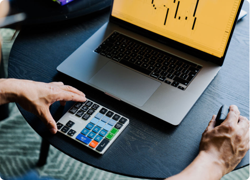 User operating the Riskeys Smart Trading Keypad next to a laptop displaying trading charts and data.